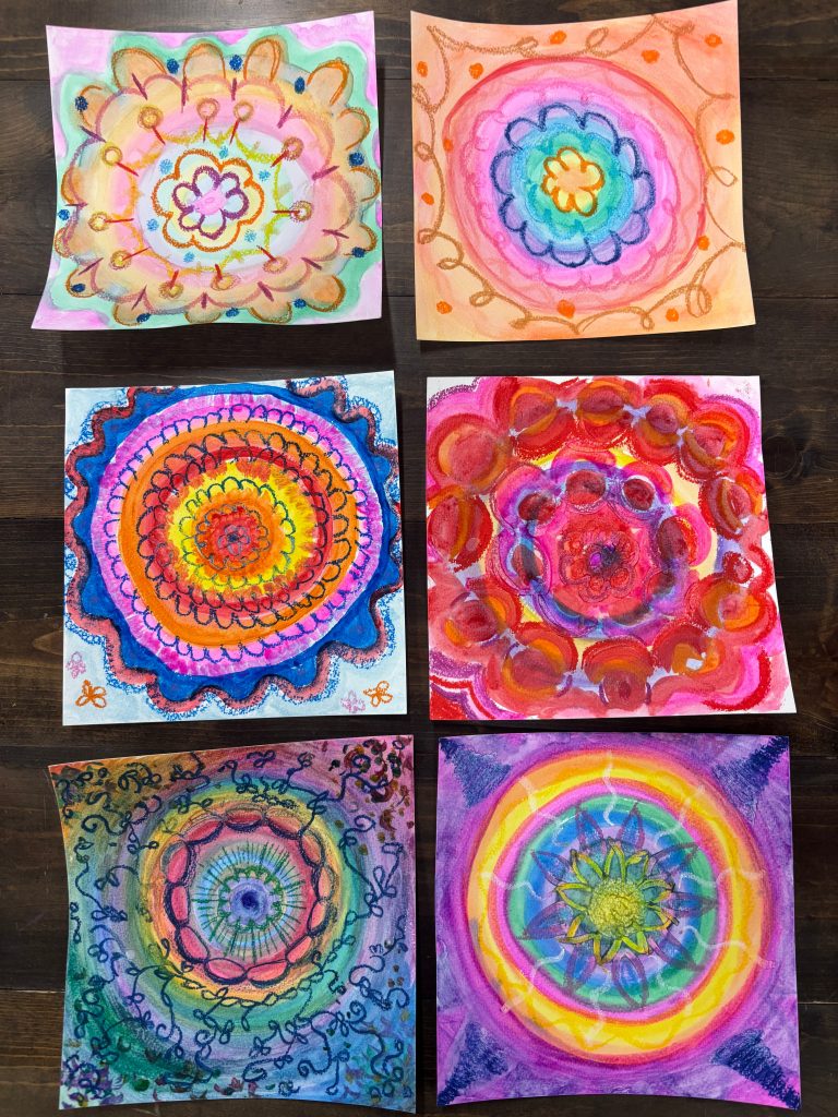 Six hand-drawn mandala artworks arranged in a grid on a wooden surface, each featuring vibrant, concentric circular floral patterns created with watercolor and crayon in a variety of bold color combinations including pink and orange, blue and orange, red and pink, and rainbow hues.